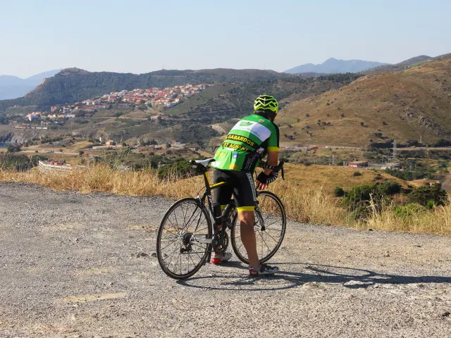 Cycliste à l’arrêt avec un vélo de route sur une route en hauteur, regardant un village et des collines en arrière-plan.