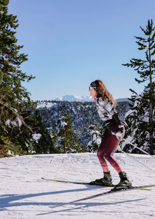 Femme pratiquant le ski de fond en technique skating sur une piste enneigée à La Llose, entourée de sapins chargés de neige, Pyrénées Catalanes