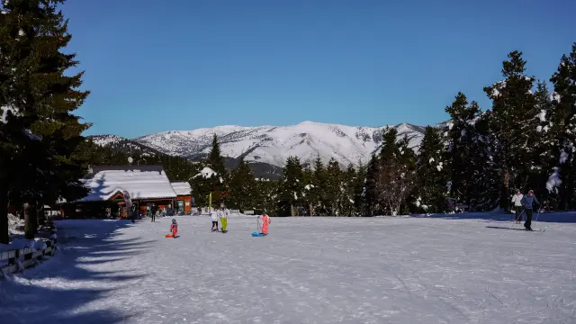 Enfants en luge colorée sur la neige devant le chalet-restaurant de La Llose, avec les sommets enneigés des Pyrénées Catalanes en arrière-plan