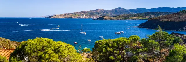 Vue sur une baie méditerranéenne avec plusieurs bateaux en mer, entourée de collines et de végétation.