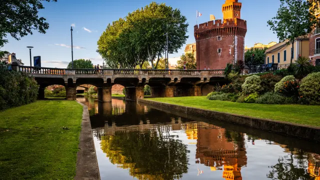 Castillet, symbole de la ville, au dessus du canal de la Basse avec reflet de son donjon dans l'eau en fin de journee aux dernieres rayons de soleil orange sur son sommet depuis le quai Vauban en Centre Ville de Perpignan dans le departement des Pyrenees-Orientales dans le sud de la France le 13 mai 2026. Decouverte touristique de Perpignan, metropole catalane du Sud de la France.