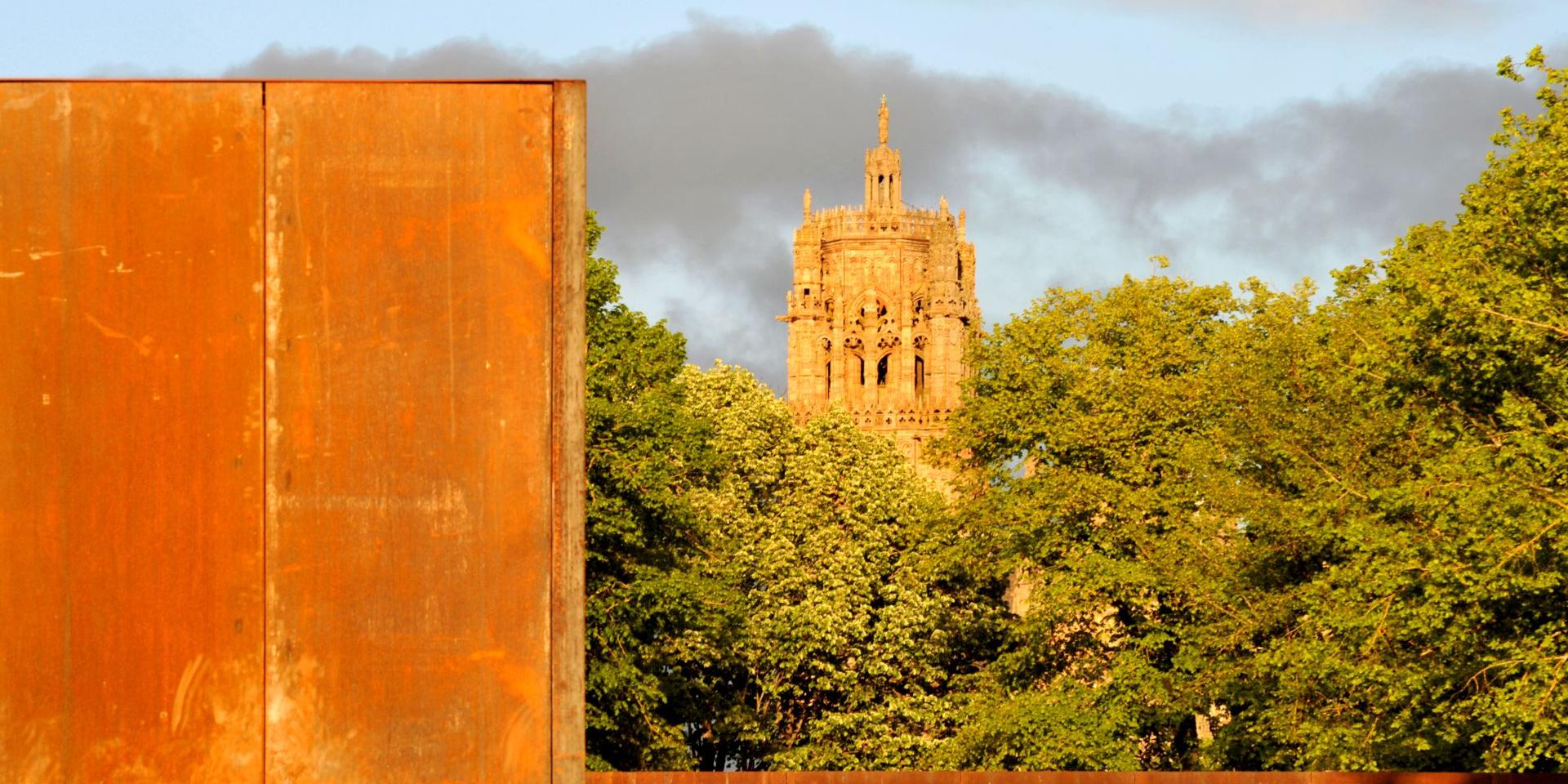 Acier Corten du musée Soulages au premier plan puis vue sur le clocher de Rodez au travers d'arbres