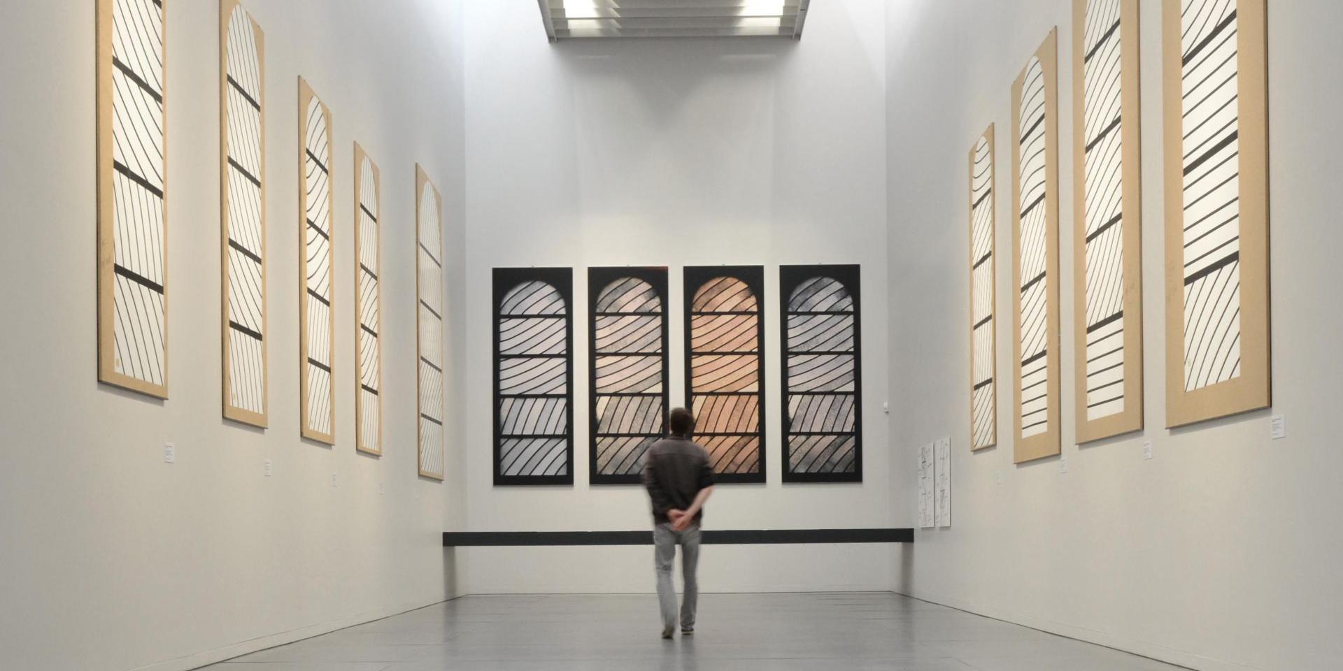 Personne au centre de la Salle de préparation aux vitraux de Conques avec des cartons aux murs et des photos du rendu final selon la luminosité
