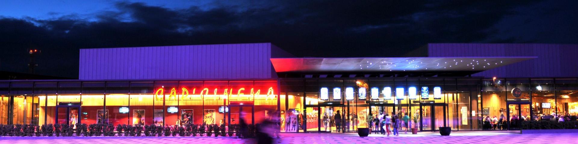 Personne marchant sur l'esplanade des ruthènes, avec un éclairage violet, devant la vitrine du Cinéma de Rodez