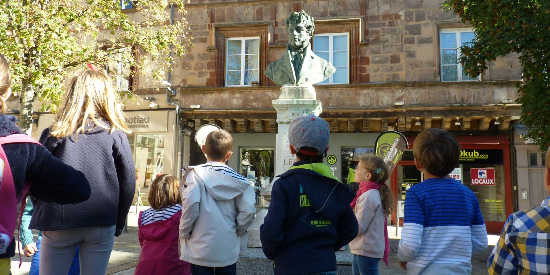 Groupe d'enfants en visite guidée, devant une sculpture sur la place du Bourg