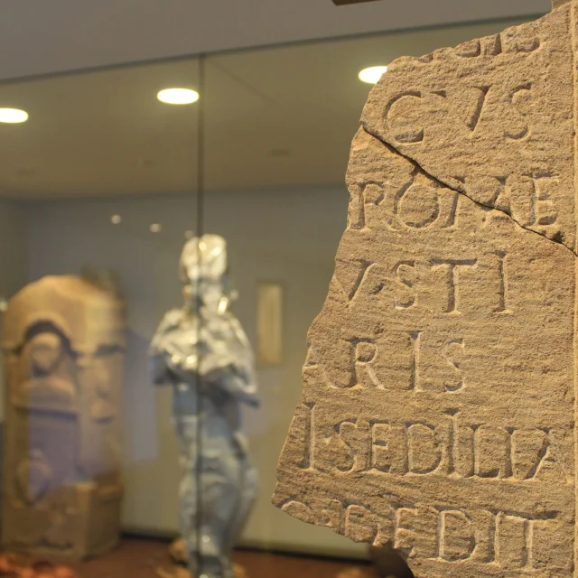 Morceau de pierre gravé avec des écritures, devant une vitrine d'objets archéologiques, au musée Fenaille