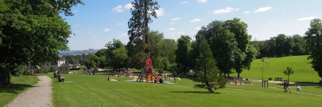Personnes se délassant au soleil sur la pelouse tout surveillant leurs enfants en train de jouer aux jeux en bois du Domaine de Vabre