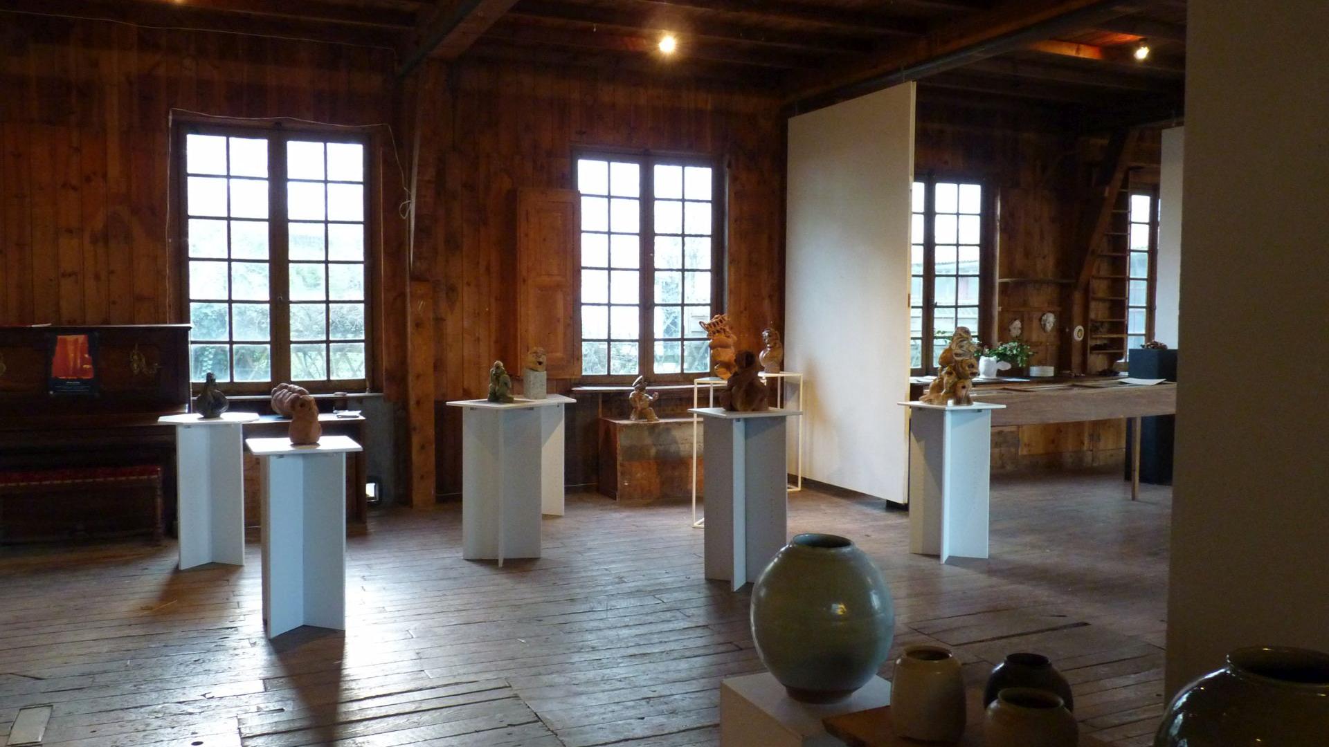 Exposition de sculptures en terre sur des tables hautes carrés blanches, dans la salle lambrissée de La Menuiserie