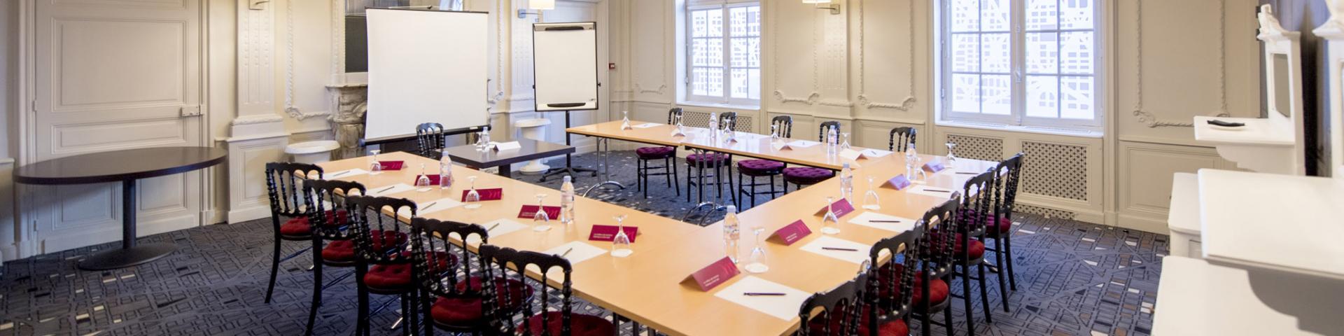 Salle de réunion en forme de U, avec des tables et des chaises en bois pour quinze personnes, dans une salle blanche aux luminaires modernes de l'hôtel Mercure
