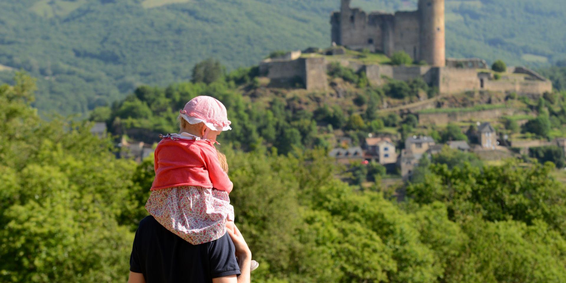 Un homme avec une petite fille sur ses épaules face à la vue sur la forteresse de Najac et la nature environnante