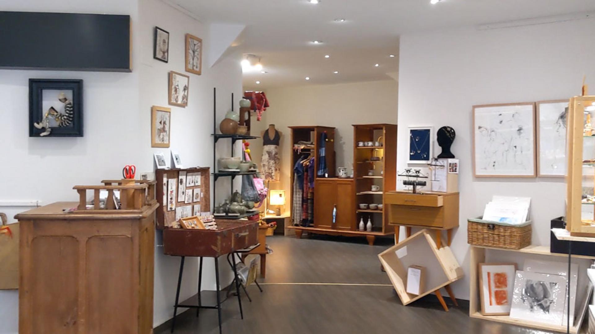 Intérieur cosy de la boutique M'Art In Boutik avec des meubles en bois pour exposer les objets en vente, et des cadres aux murs