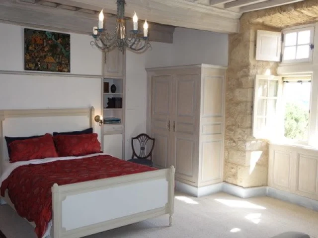 Chambre double du château de Balsac avec un lit au par-dessus rouge, une armoire blanche en bois, et un luminaire style bougies, devant une fenêtre ouverte