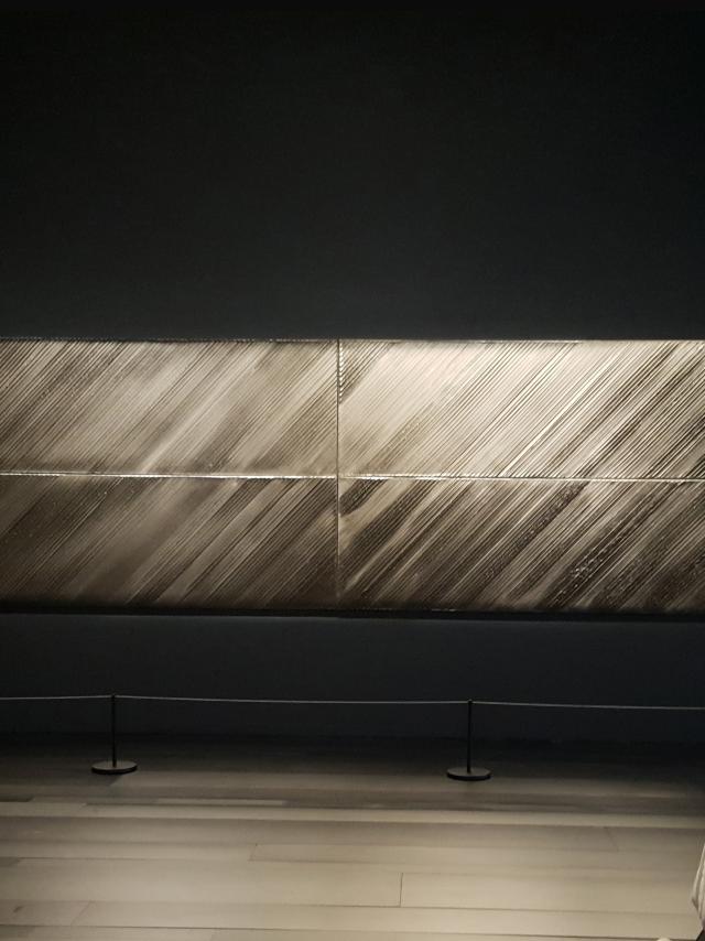 Personne qui admire un tableau horizontal Outrenoir de Pierre Soulages exposé dans une salle du musée