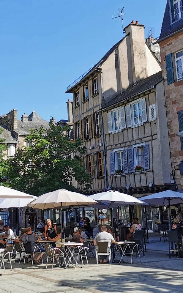 Personnes assises à la terrasse d'un café, sous des parasols blancs, sur la place du Bourg, devant des maisons à colombages