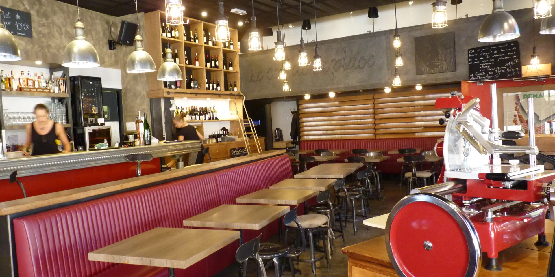 Intérieur du restaurant Le Coq de la Place style bistro avec ses tables en bois le long d'une banquette en cuir rouge et ses chaises en fer