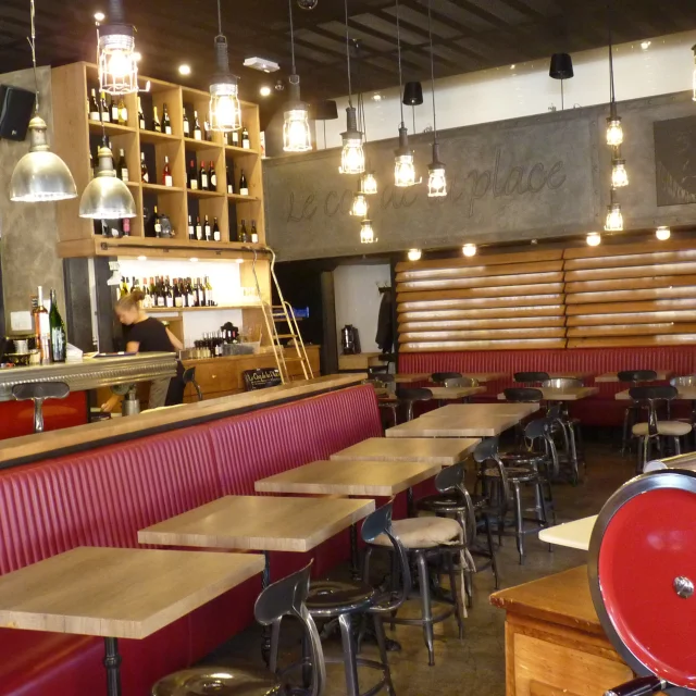 Intérieur du restaurant Le Coq de la Place style bistro avec ses tables en bois le long d'une banquette en cuir rouge et ses chaises en fer