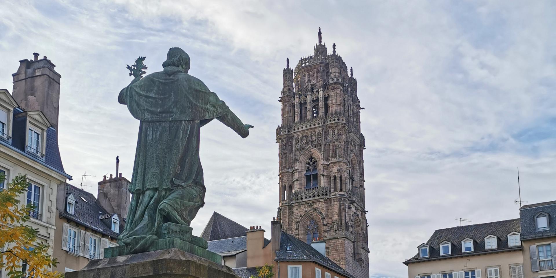 Dos d'une statue en bronze avec un doigt désignant le clocher de la cathédrale