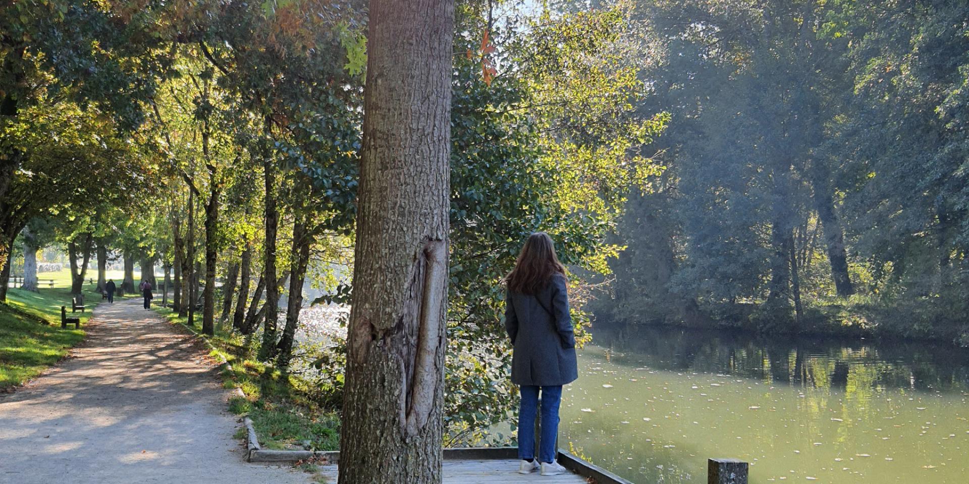 Au bord d'un chemin de promenade entre les arbres, au bord de l'eau, personne sur un ponton de bois de dos, qui regarde la rivière Aveyron