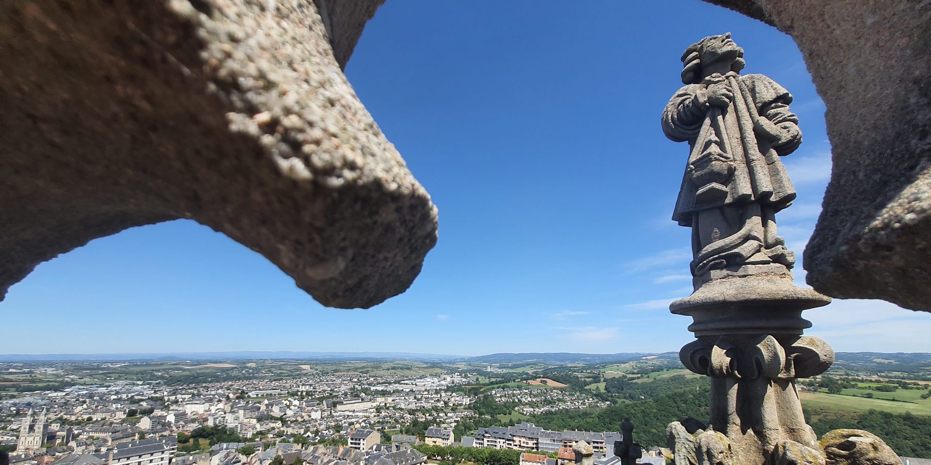 Au sommet du clocher de la cathédrale de Rodez, vue sur un ange thuriféraire sculpté dos à la ville, à travers une fenêtre de pierre