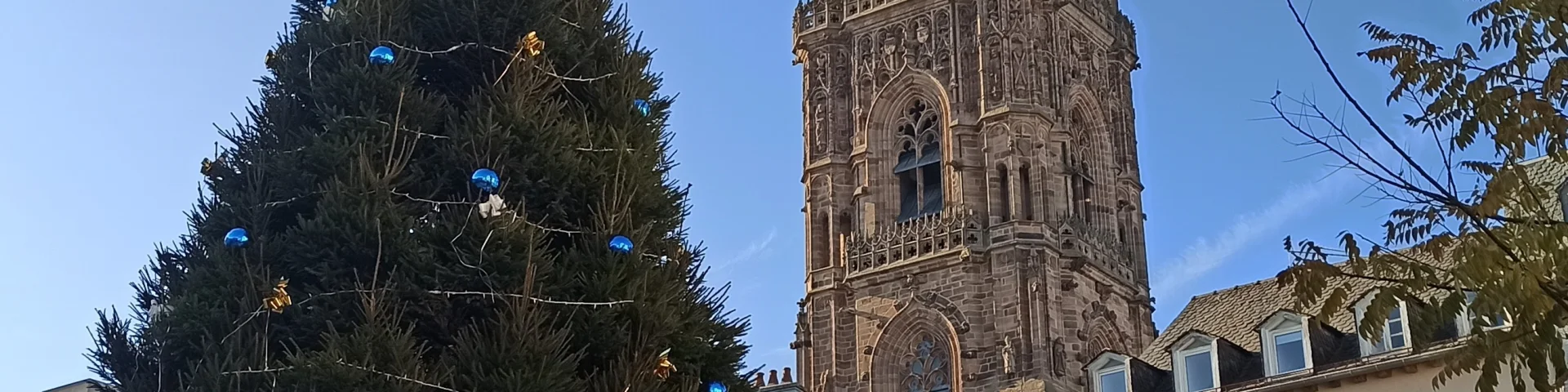 Sapin géant décoré pour Noël devant le clocher de la cathédrale, sous un ciel bleu