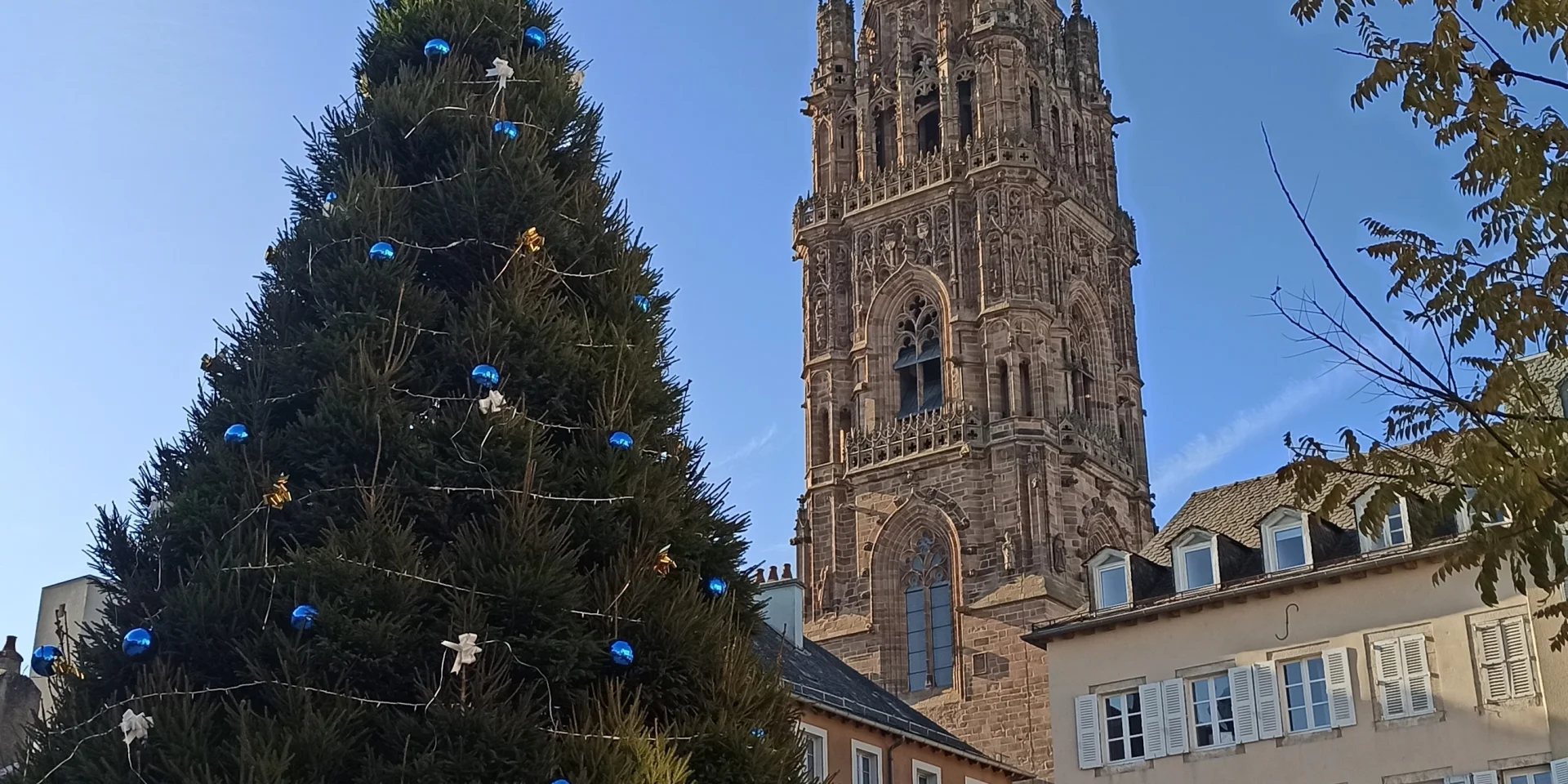 Sapin géant décoré pour Noël devant le clocher de la cathédrale, sous un ciel bleu