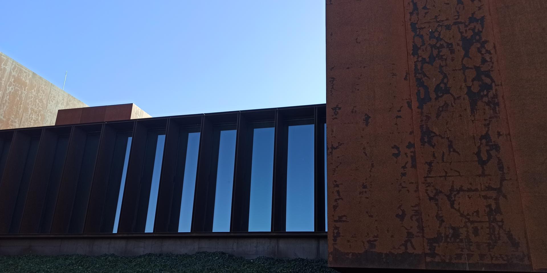 Jeu de matières et de contrastes : le verre des fenêtres avec un reflet bleu du ciel et les murs en acier Corten aux teintes de couleur rouille, au musée Soulages