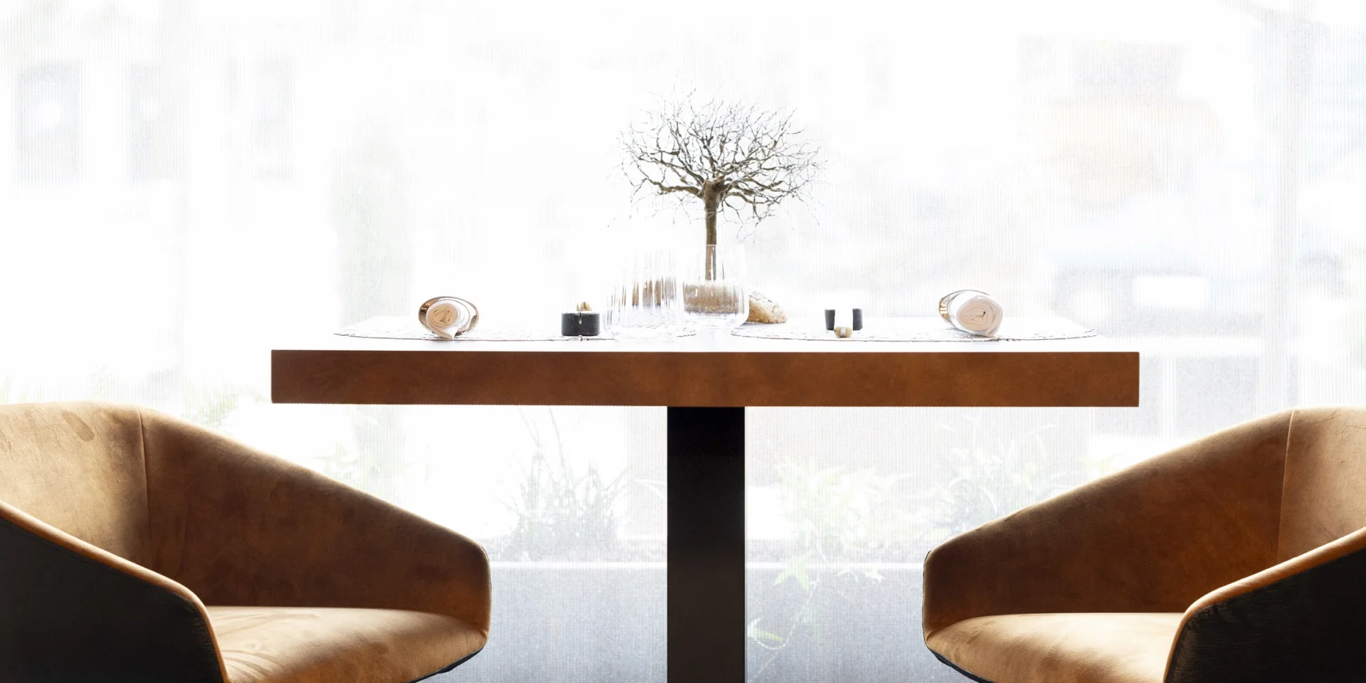 Table en bois dressée pour deux personnes avec deux fauteuils au restaurant Hervé Busset