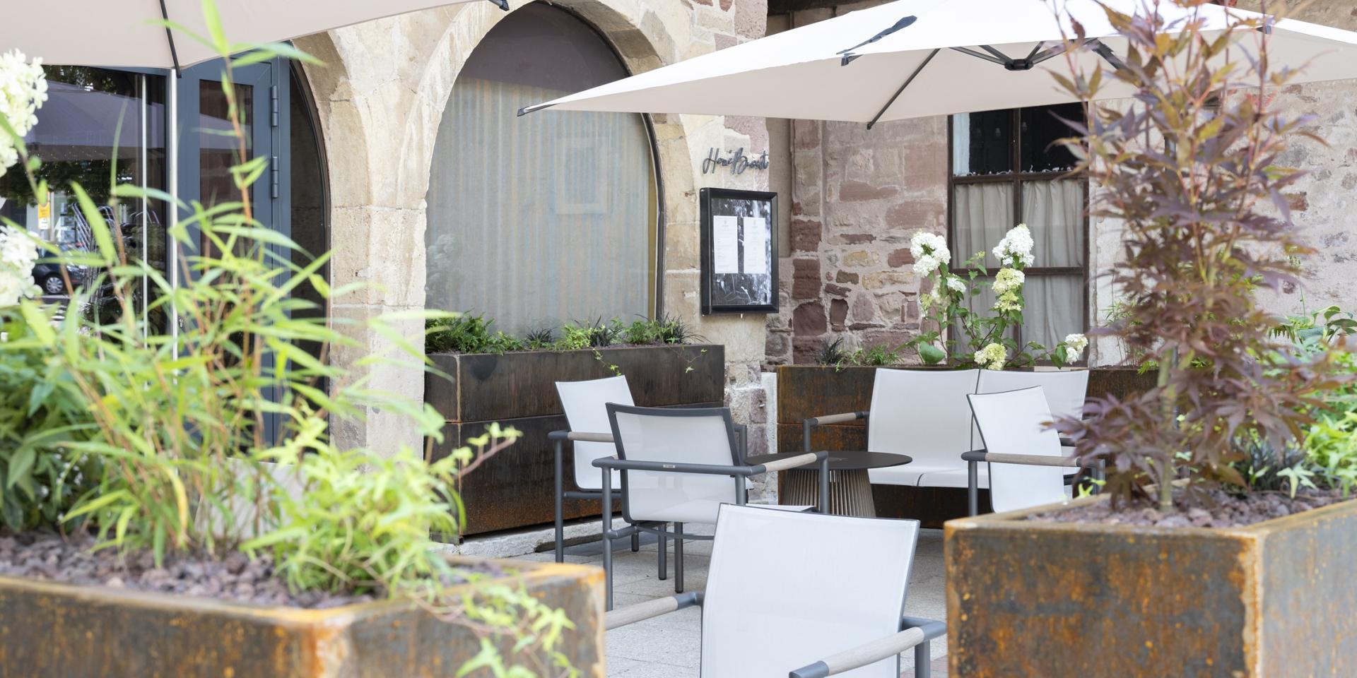 Terrasse du restaurant Hervé Busset avec du mobilier blanc de salon de jardin, entre des jardinières fleuries en acier Corten