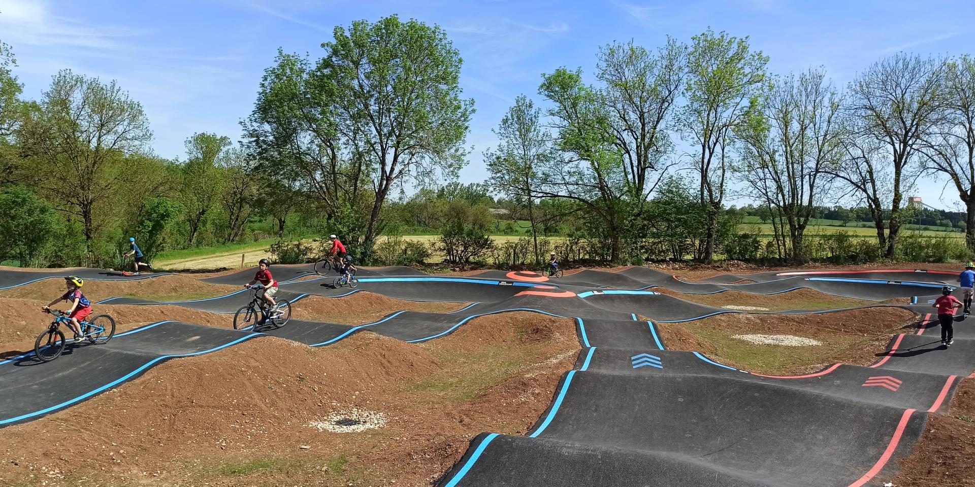 Enfants à vélo ou à trotinette sur les pistes gourdonnées et vallonnées bleu ou rouge d'un pumptrack