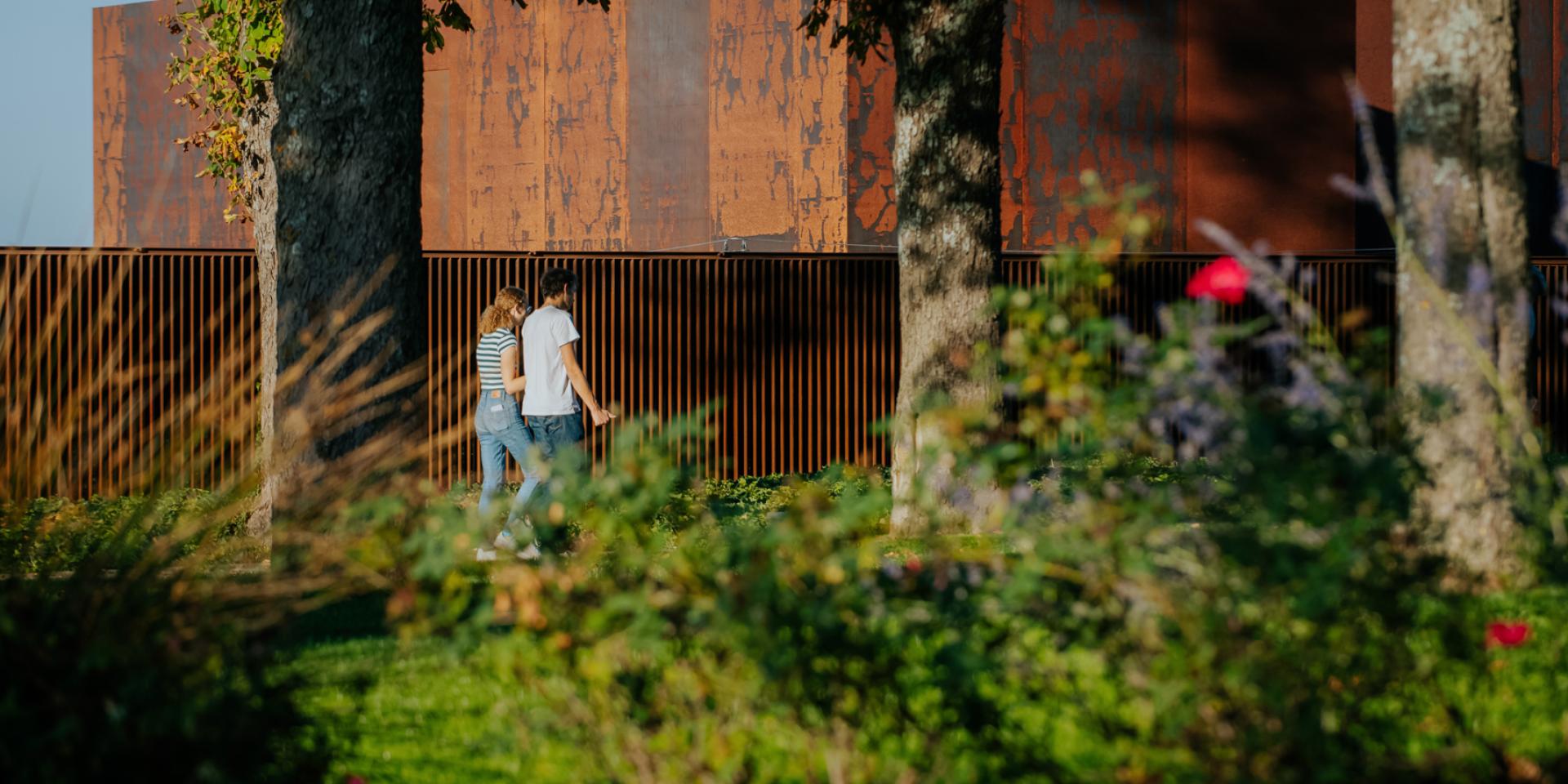 Couple se promenant dans le jardin à côté du musée Soulages au bardage en acier Corten couleur rouille