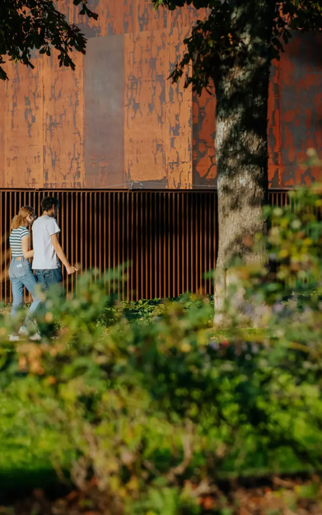 Couple se promenant dans le jardin à côté du musée Soulages au bardage en acier Corten couleur rouille