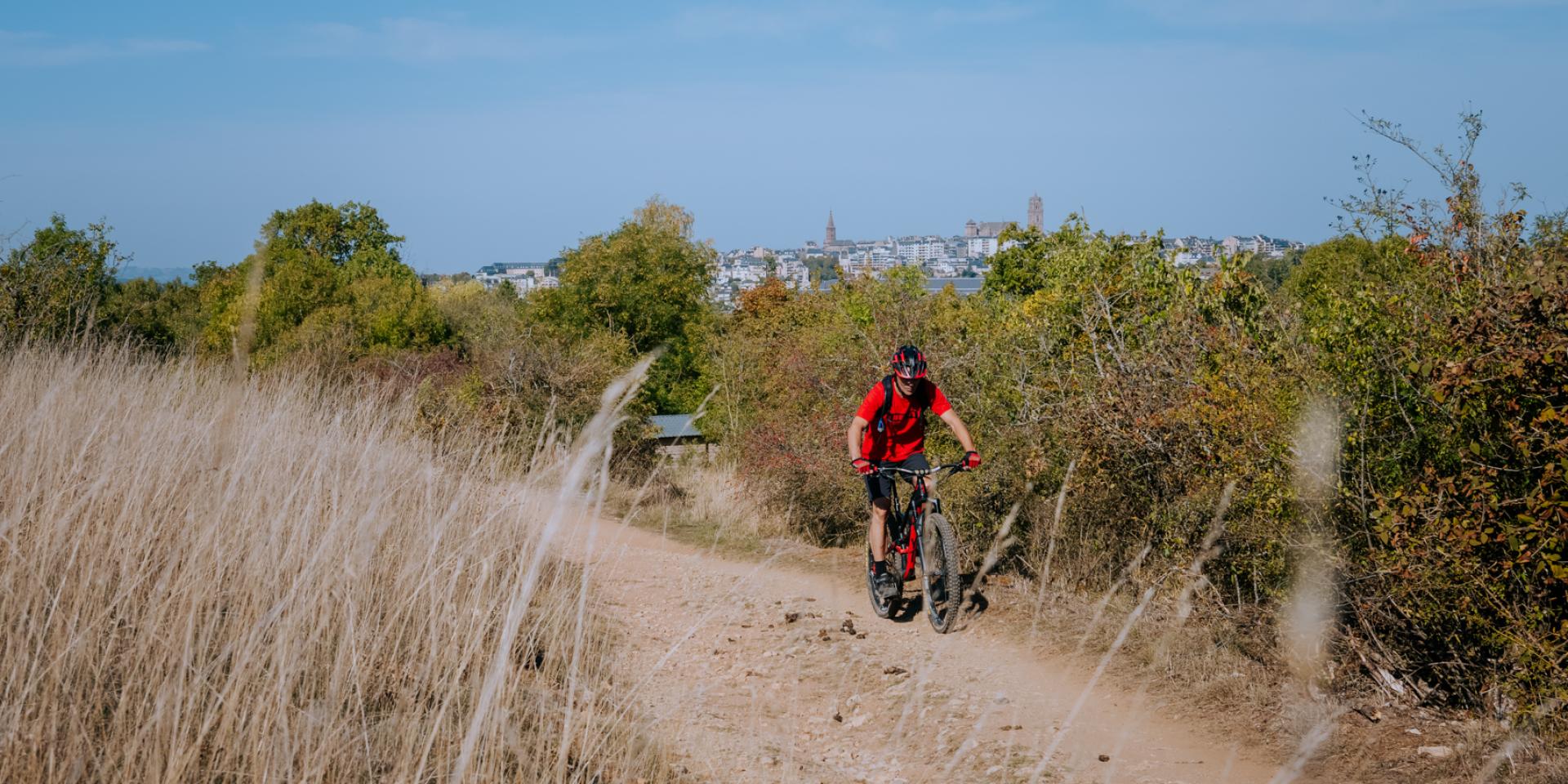 Personne à VTT sur un chemin de terre dos à la cathédrale de Rodez aperçue en hauteur