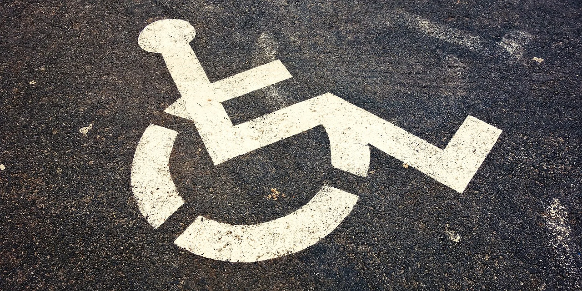Peint en blanc, sigle au sol sur une place de parking goudronné, signifiant un emplacement pour personne à mobilité réduite