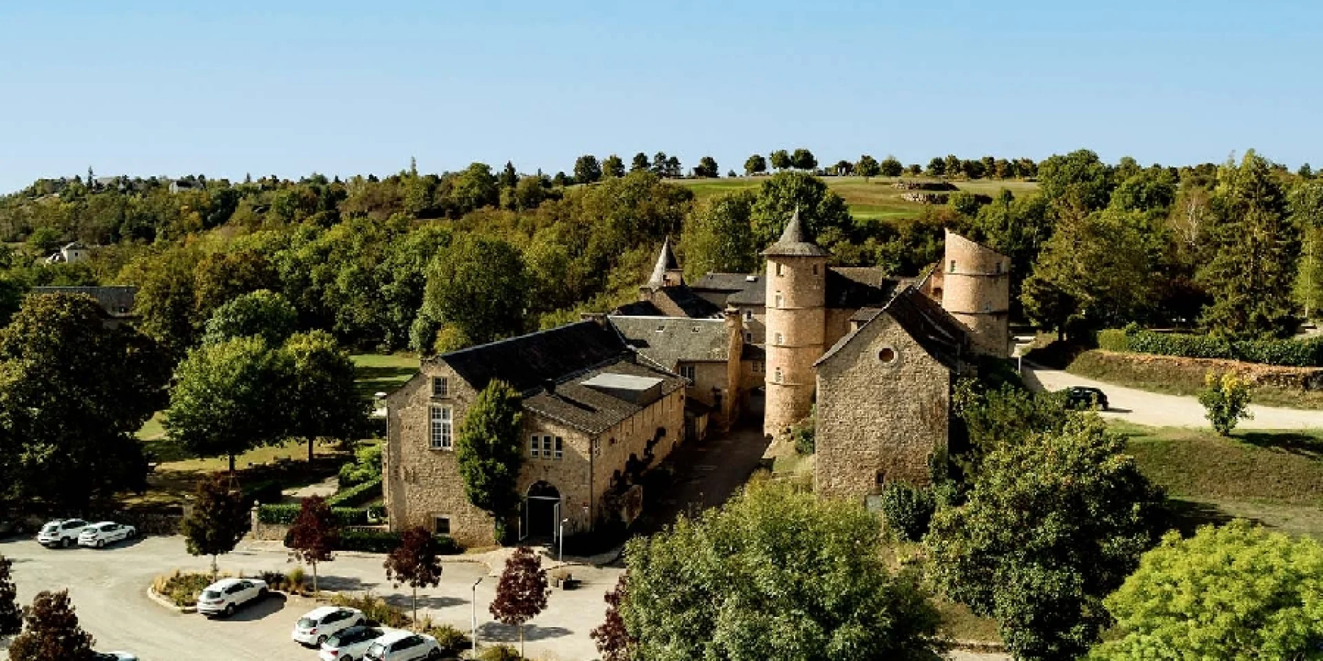 Vue aérienne du château de Fontanges, ses tourelles et son parking à proximité, entouré d'espaces verts