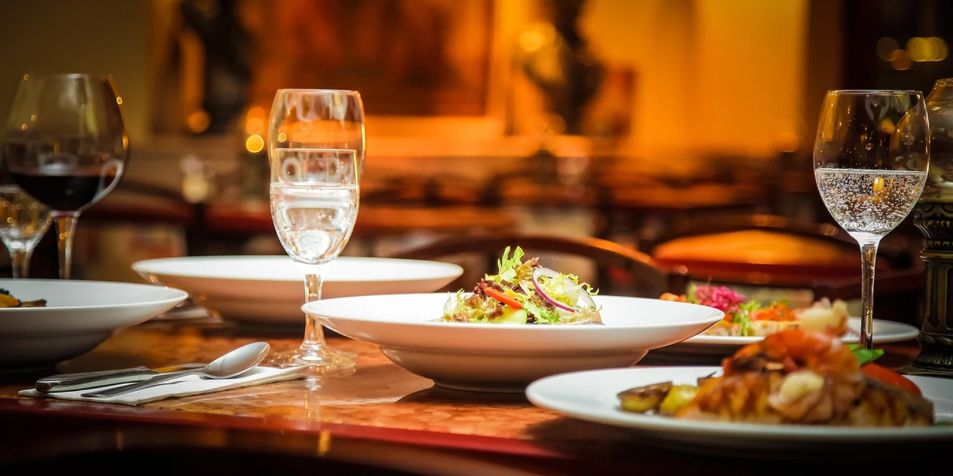 Table de restaurant avec des assiettes garnies, des couverts, serviettes, et verres à pied remplis d'eau pétillante