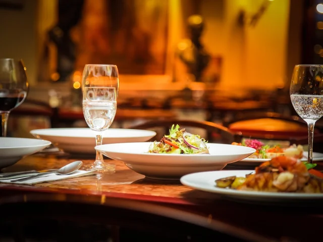 Table de restaurant avec des assiettes garnies, des couverts, serviettes, et verres à pied remplis d'eau pétillante