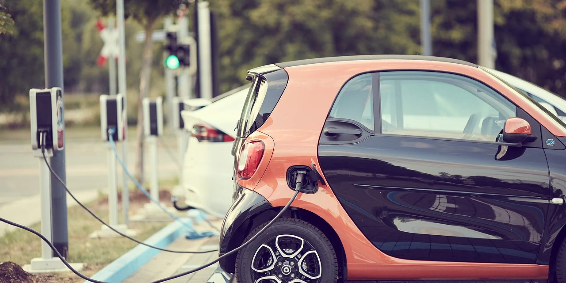 Voitures électriques reliées à une borne de recharge par un câble, sur un parking extérieur dédié