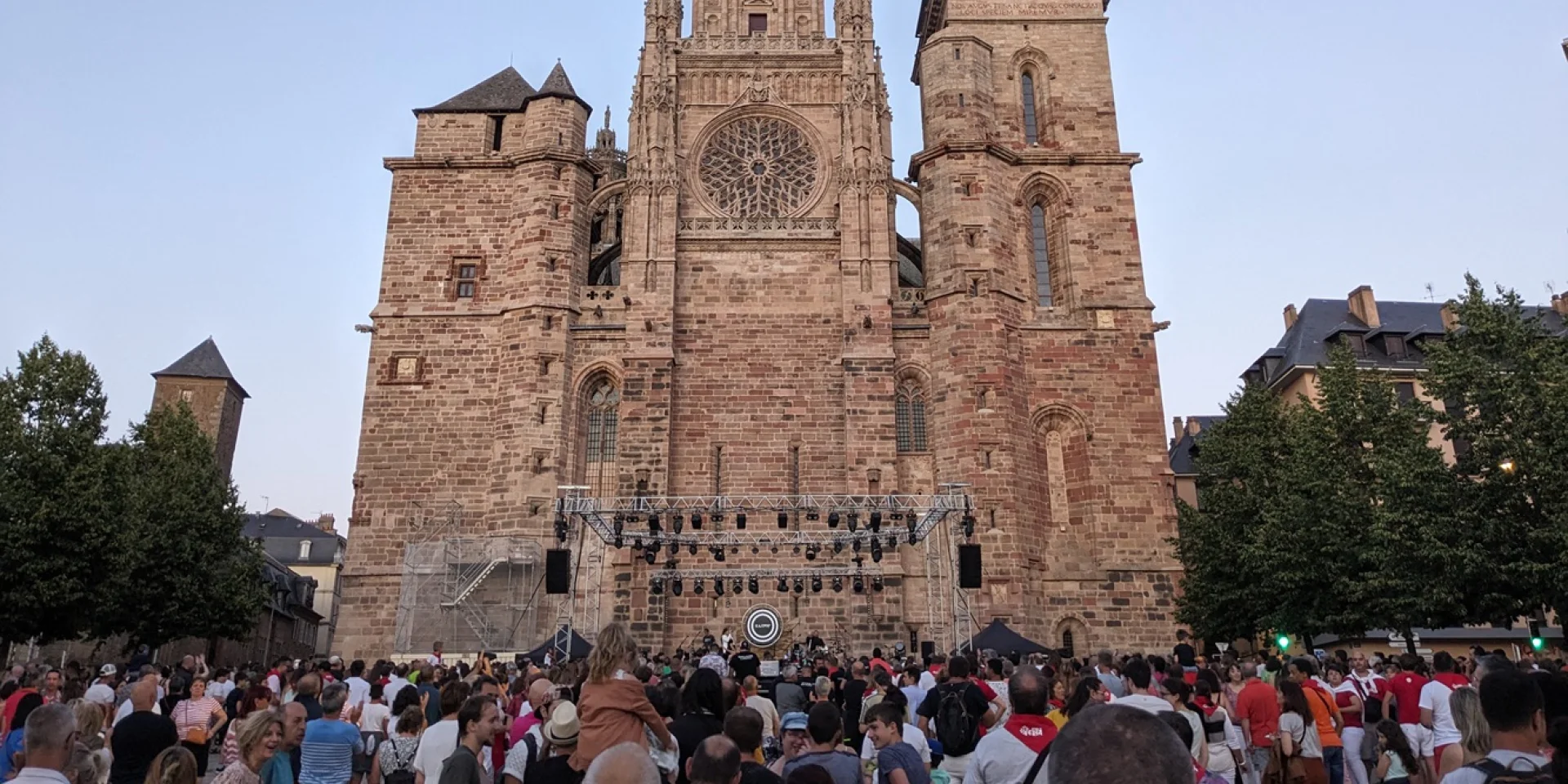 Foule de personnes devant une scène disposée devant la cathédrale, en fin de journée