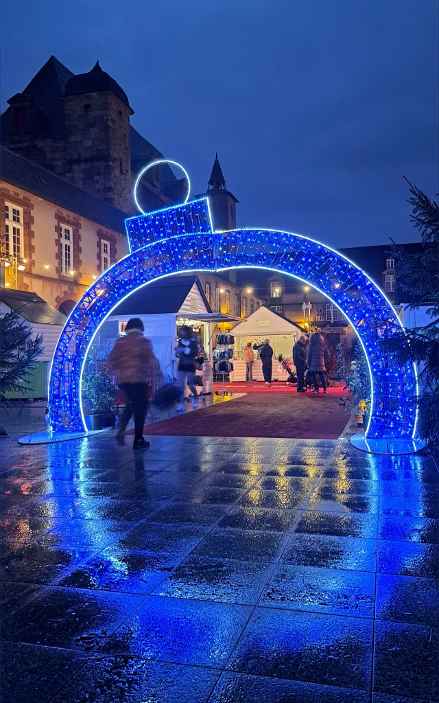 Illuminations sous forme de boule de Noël sous laquelle une personne passe, à l'entrée du marché de Noël de Rodez
