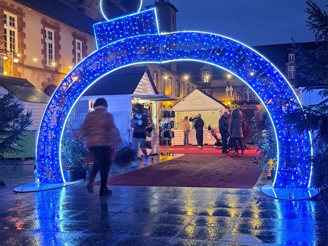 Illuminations sous forme de boule de Noël sous laquelle une personne passe, à l'entrée du marché de Noël de Rodez
