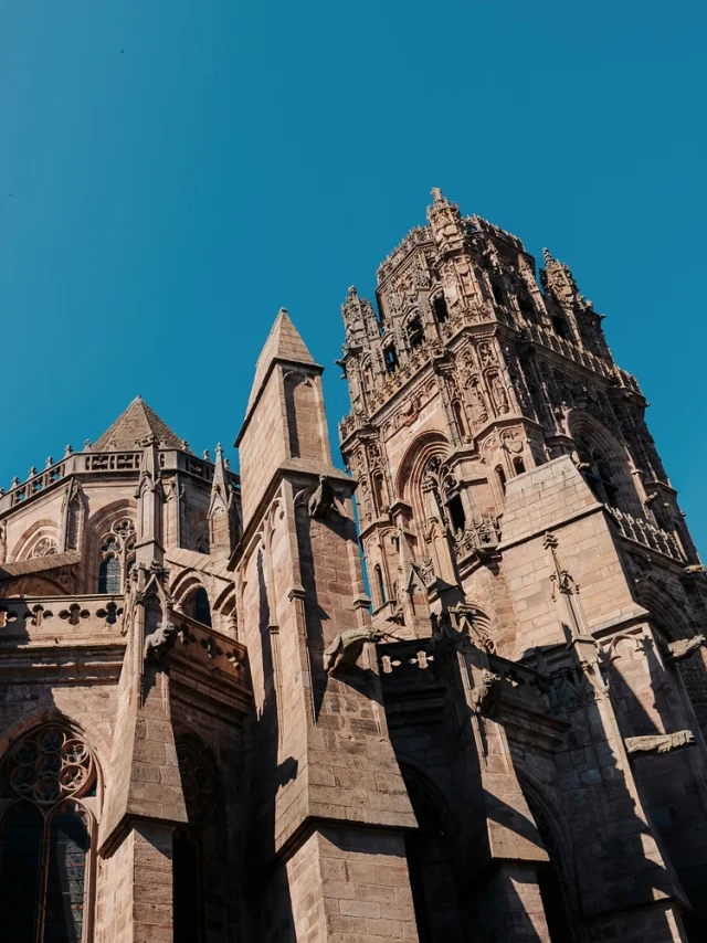 Chevet de la cathédrale avec ses nombreuses gargouilles de pierre, ses piliers, ses sculptures, devant le clocher plus haut, sous un ciel bleu