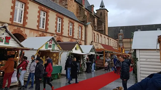 Personnes déambulant sur le tapis rouge au marché de Noël de Rodez, devant les chalets en bois installé sur la place Foch