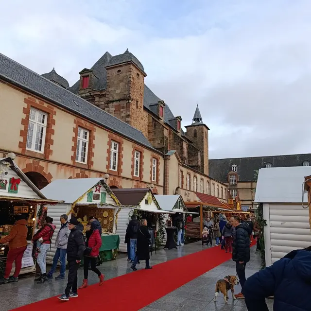 Personnes déambulant sur le tapis rouge au marché de Noël de Rodez, devant les chalets en bois installé sur la place Foch
