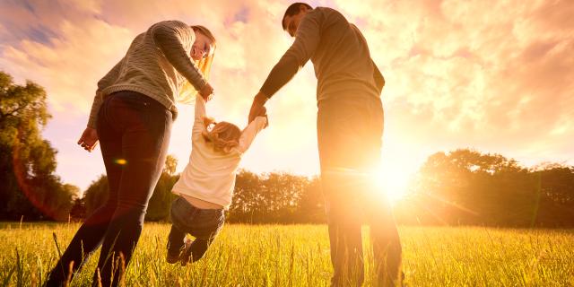 Happy family in the park evening light. The lights of a sun. Mom, dad and baby happy walk at sunset. The concept of a happy family.Parents hold the baby's hands.