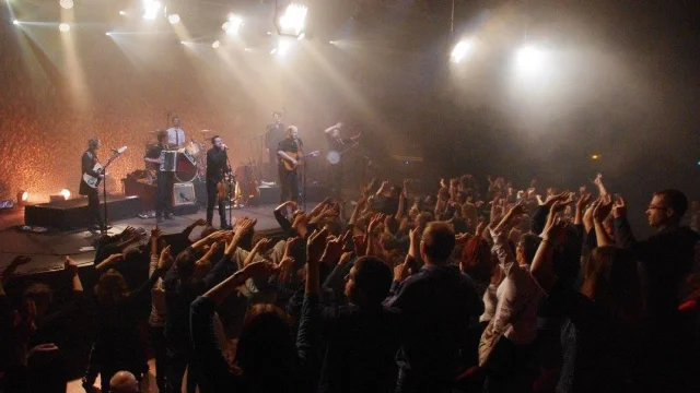 photo d'un concert avec chanteur, guitaristes et batterie sur scène devant une foule les bras levés