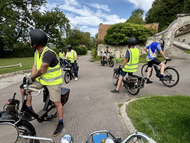 Groupe de participants en Solex traversant un village normand