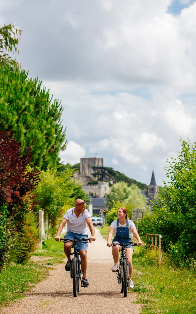 Deux personnes en vélo sur l'itinéraire Coeur de France à Vélo. Le donjon de Montrichard est en fond de la photograhie.