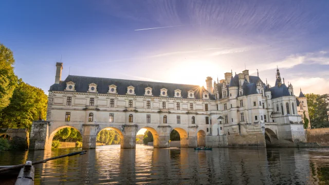 Une fin de journée ensoleillée, vue sur le Château de Chenonceau et sa galerie traversant le Cher depuis un bateau qui navigue sur le Cher.