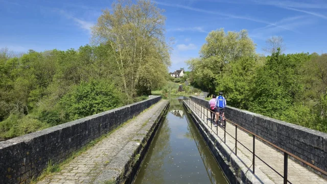 Sous un grand soleil de printemps, deux cyclistes son t de dos et traversent le pont canal de Châtillon-sur-Cher.