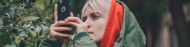 Une femme abritée sous une capuche prend une photo avec son téléphone portable en forêt